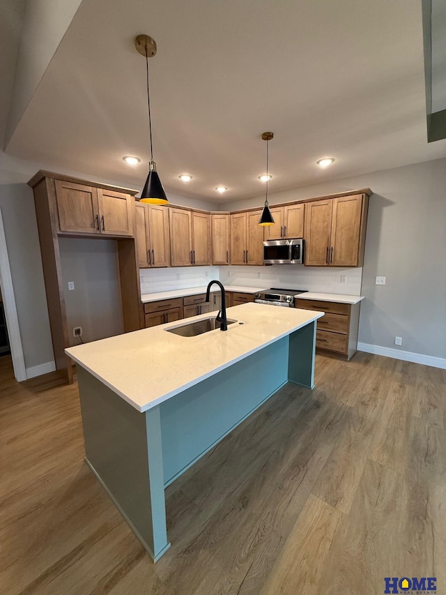 kitchen with stainless steel appliances, a kitchen island with sink, hanging light fixtures, and sink