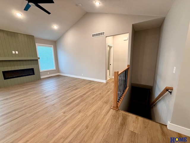 living room with light wood-type flooring, vaulted ceiling, a large fireplace, and ceiling fan