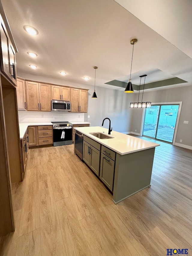 kitchen featuring decorative light fixtures, sink, a kitchen island with sink, light wood-type flooring, and stainless steel appliances