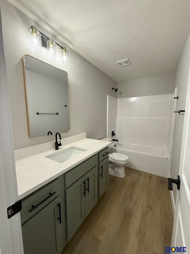 full bathroom featuring toilet, bathing tub / shower combination, hardwood / wood-style flooring, a textured ceiling, and vanity