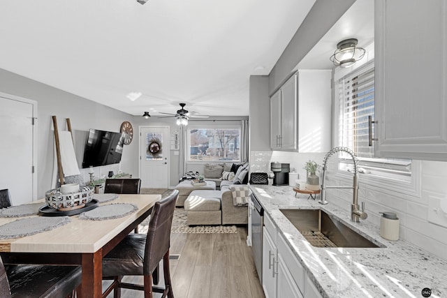 kitchen with white cabinetry, stainless steel dishwasher, light stone counters, and sink