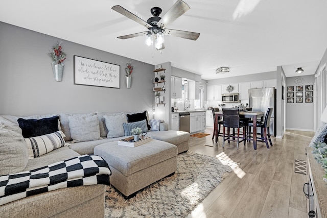 living room with ceiling fan, sink, and light wood-type flooring