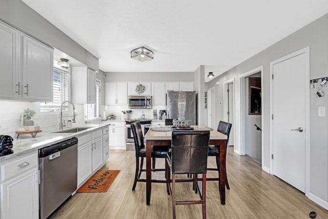 kitchen with appliances with stainless steel finishes, white cabinetry, tasteful backsplash, light hardwood / wood-style floors, and sink