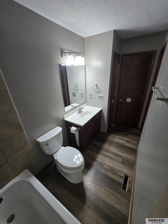 bathroom featuring a textured ceiling, wood-type flooring, vanity, a bathtub, and toilet