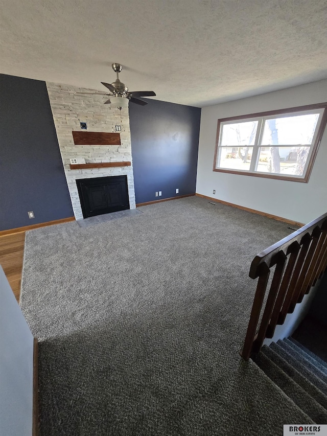 unfurnished living room featuring ceiling fan, a stone fireplace, a textured ceiling, and carpet flooring