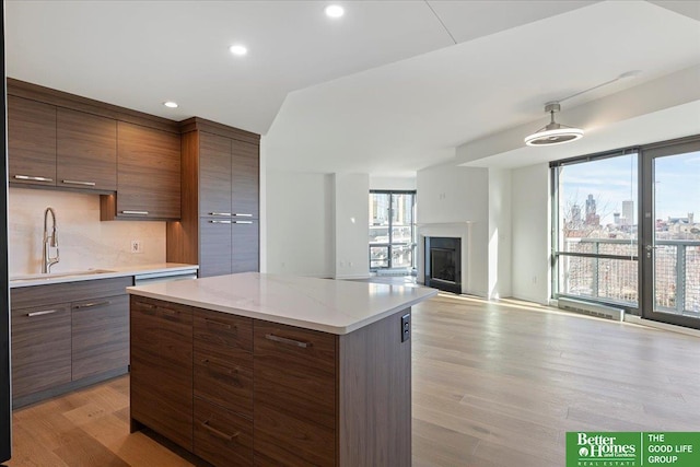 kitchen featuring dark brown cabinetry, tasteful backsplash, sink, light wood-type flooring, and light stone counters