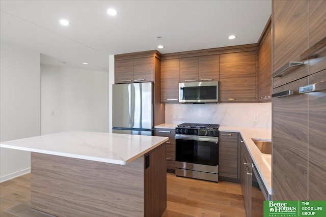 kitchen with light hardwood / wood-style floors, appliances with stainless steel finishes, decorative backsplash, a kitchen island, and sink