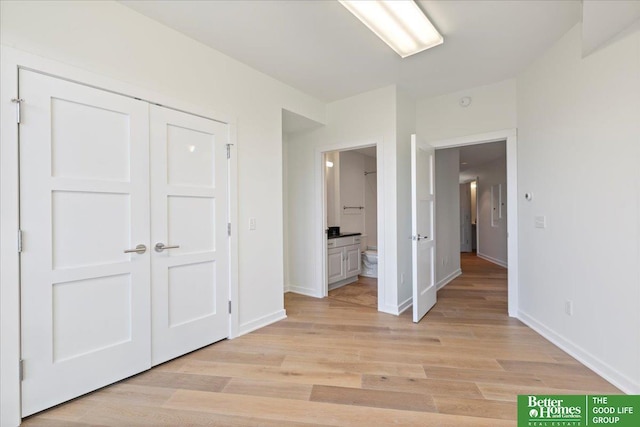 unfurnished bedroom with a closet, ensuite bathroom, and light hardwood / wood-style floors