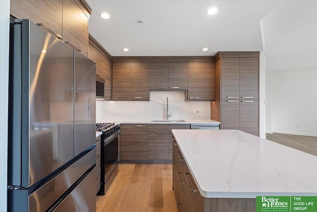 kitchen with appliances with stainless steel finishes, light hardwood / wood-style floors, sink, backsplash, and light stone counters