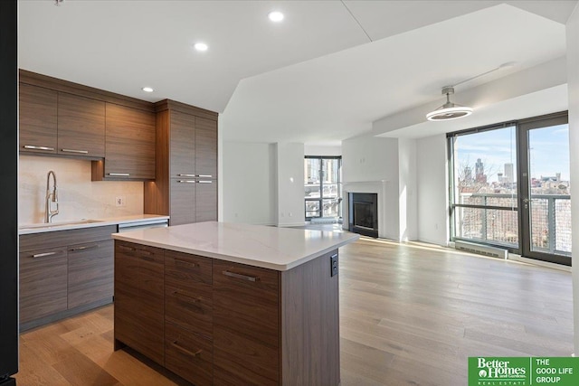 kitchen featuring a kitchen island, light hardwood / wood-style floors, sink, backsplash, and light stone counters