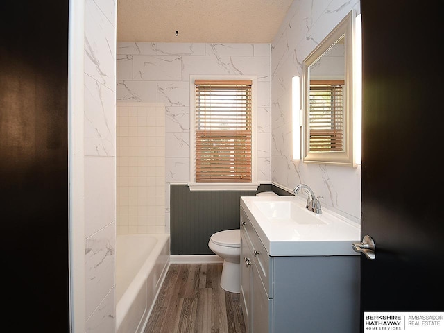 bathroom with toilet, a bathing tub, wood-type flooring, a textured ceiling, and vanity