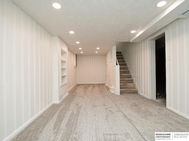 basement featuring a textured ceiling, light colored carpet, and built in shelves