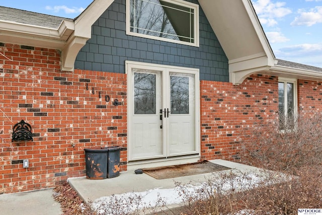 view of exterior entry with a shingled roof and brick siding