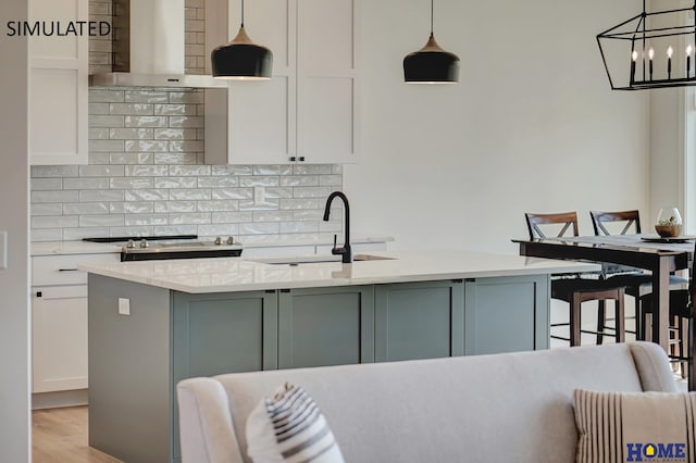 kitchen with hanging light fixtures, a kitchen island with sink, sink, and light stone counters