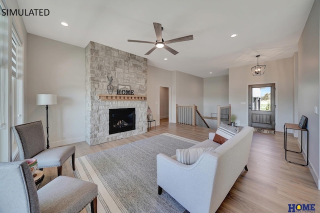 living room featuring ceiling fan with notable chandelier, a fireplace, and light hardwood / wood-style flooring