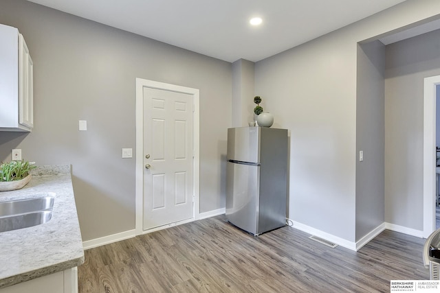 kitchen with sink, white cabinetry, light hardwood / wood-style flooring, and stainless steel refrigerator