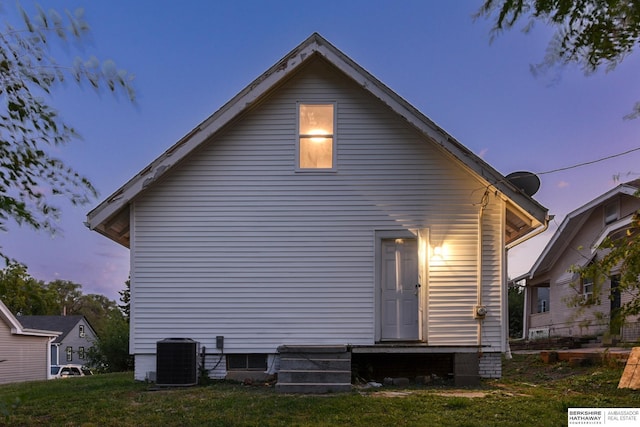 back house at dusk with central AC unit and a lawn