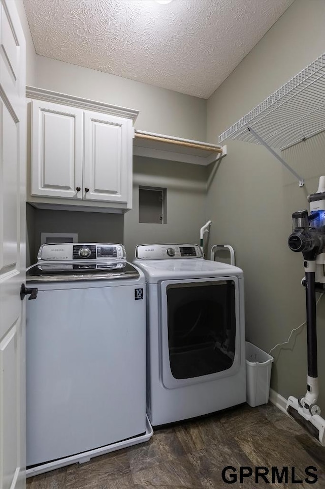 clothes washing area featuring cabinets, a textured ceiling, and washer and clothes dryer