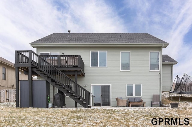 rear view of property with a trampoline and a wooden deck