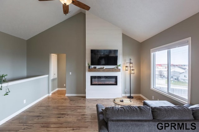 living room featuring ceiling fan, wood-type flooring, a fireplace, and high vaulted ceiling