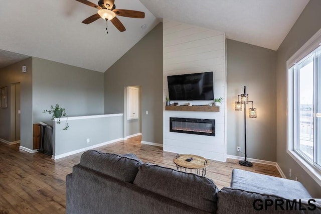 living room featuring ceiling fan, a large fireplace, hardwood / wood-style flooring, and high vaulted ceiling