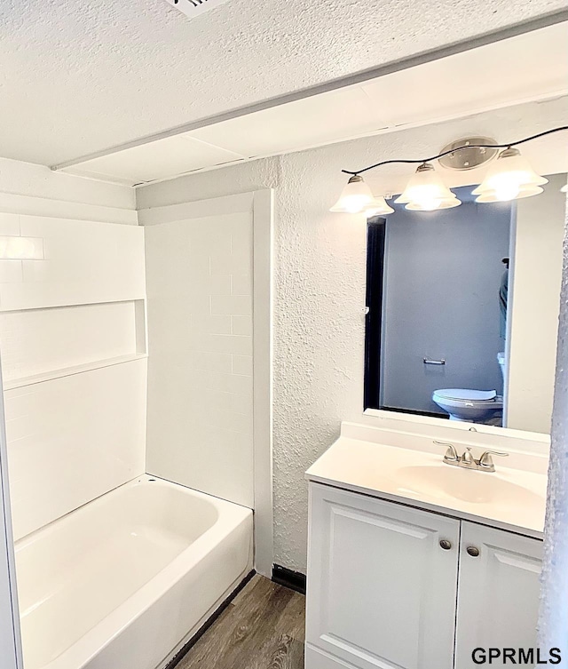 full bathroom featuring a textured ceiling, bathing tub / shower combination, wood-type flooring, vanity, and toilet