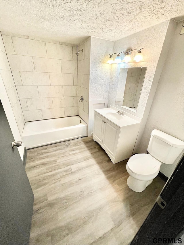 full bathroom with toilet, tiled shower / bath, wood-type flooring, a textured ceiling, and vanity