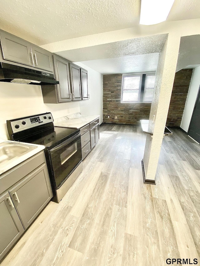 kitchen with light wood-type flooring, a textured ceiling, wooden walls, and stainless steel electric range