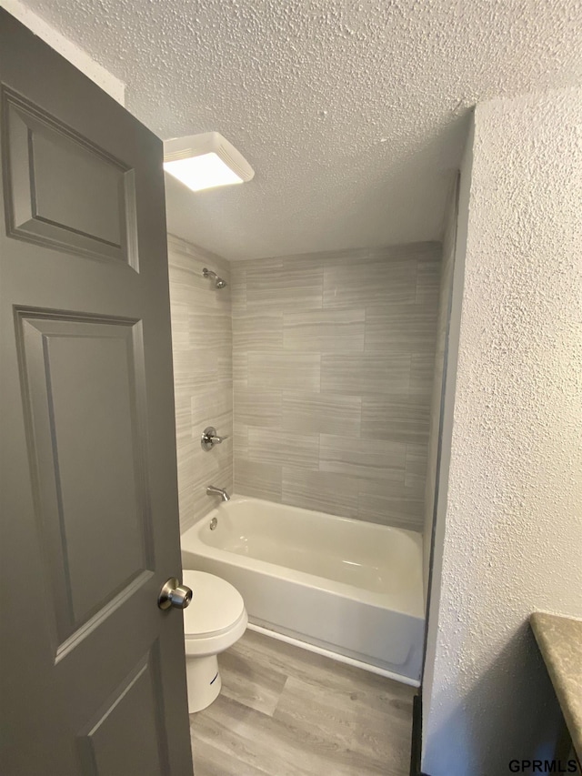 bathroom featuring hardwood / wood-style flooring, a textured ceiling, toilet, and tiled shower / bath