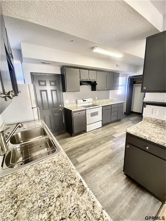 kitchen with a textured ceiling, sink, light wood-type flooring, and white appliances