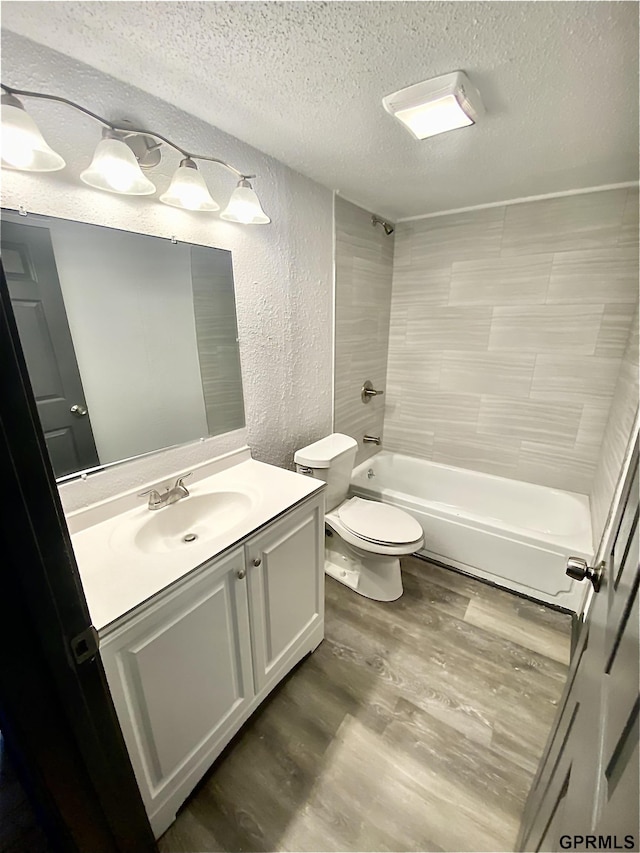 full bathroom featuring toilet, tiled shower / bath combo, hardwood / wood-style flooring, a textured ceiling, and vanity