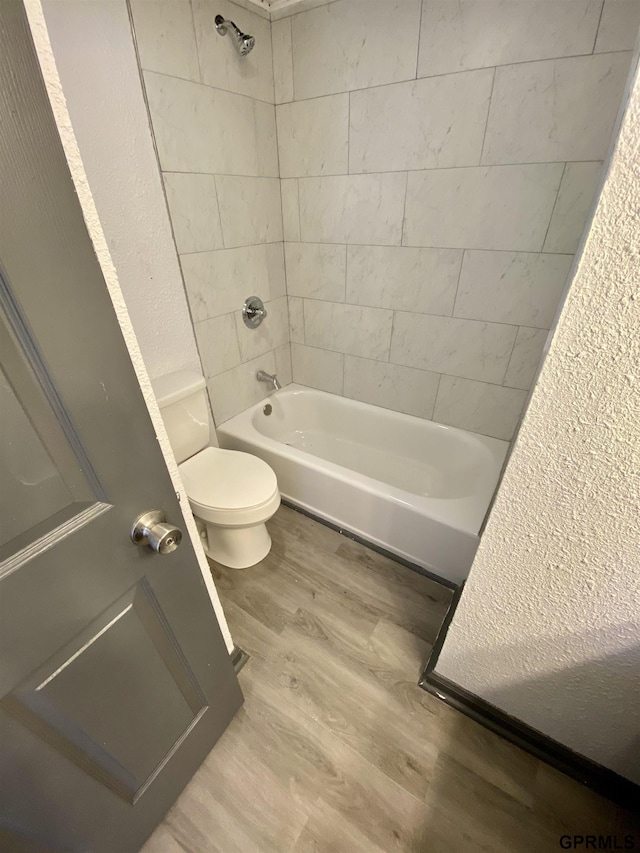 bathroom featuring toilet, tiled shower / bath, and wood-type flooring