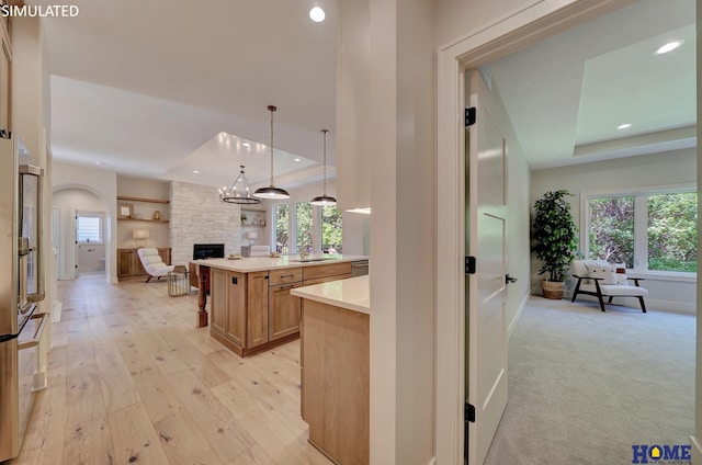 kitchen with light colored carpet, a fireplace, a tray ceiling, hanging light fixtures, and stainless steel appliances