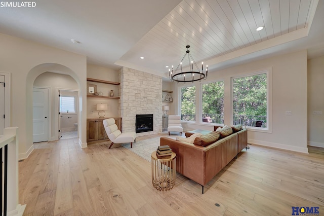 living room featuring a stone fireplace, light hardwood / wood-style floors, a notable chandelier, wooden ceiling, and a tray ceiling