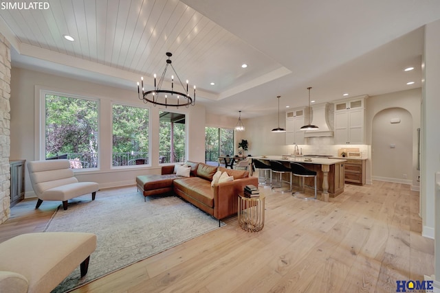 living room featuring a raised ceiling, a notable chandelier, sink, and light hardwood / wood-style floors