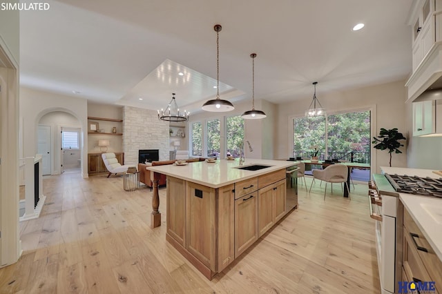 kitchen with a stone fireplace, appliances with stainless steel finishes, light wood-type flooring, a large island with sink, and sink