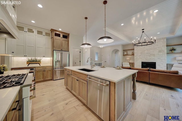 kitchen featuring appliances with stainless steel finishes, decorative light fixtures, an island with sink, sink, and light hardwood / wood-style flooring