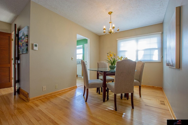 dining space with a notable chandelier, a textured ceiling, and light hardwood / wood-style flooring