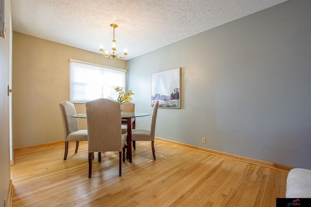 dining space with a textured ceiling, light hardwood / wood-style flooring, and a chandelier