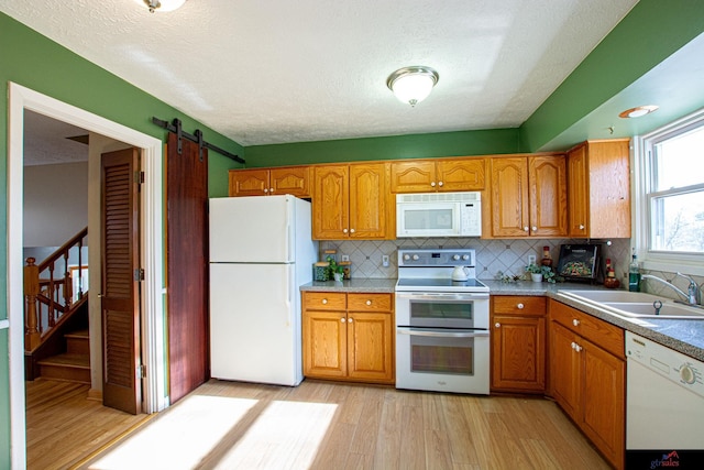 kitchen featuring a barn door, backsplash, white appliances, light wood-type flooring, and sink