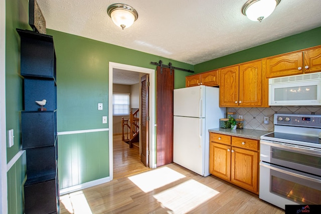 kitchen featuring a barn door, backsplash, white appliances, light wood-type flooring, and a textured ceiling