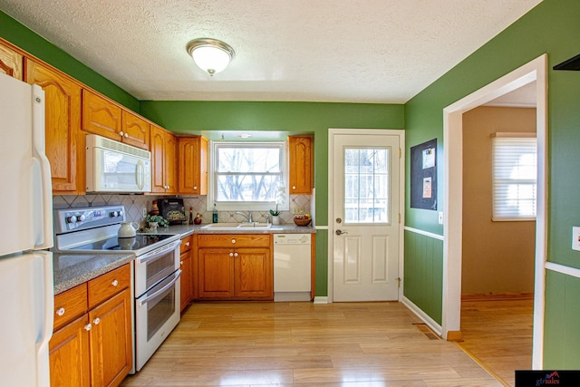 kitchen featuring sink, white appliances, backsplash, and light wood-type flooring