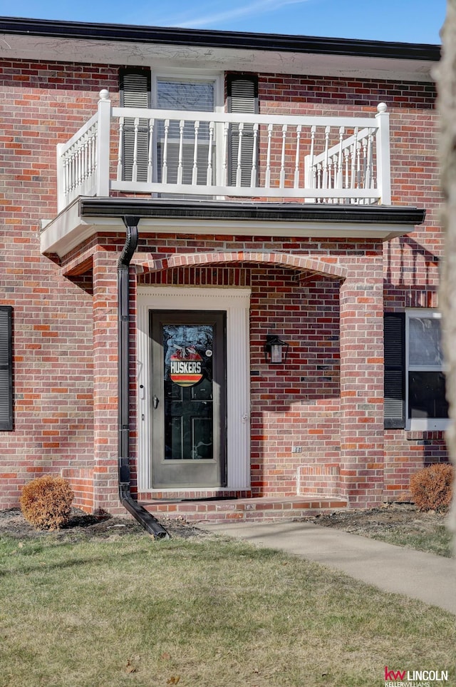 view of exterior entry featuring a balcony and a lawn