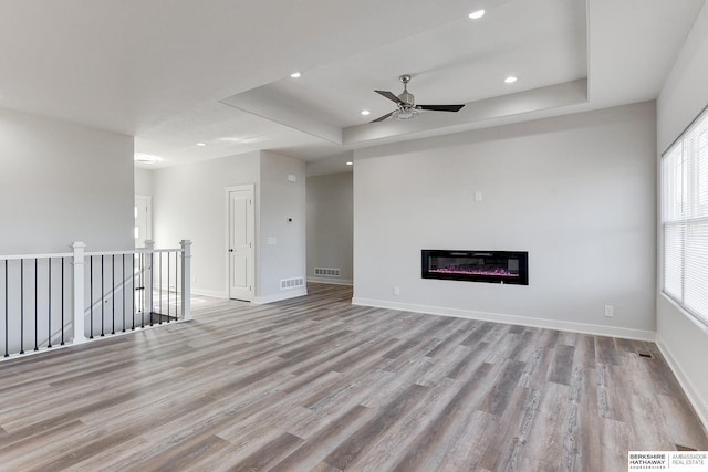 unfurnished living room with ceiling fan, light hardwood / wood-style flooring, and a tray ceiling