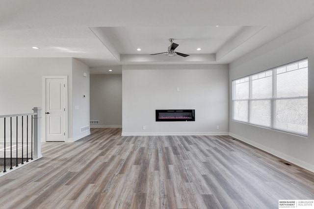 unfurnished living room featuring ceiling fan, light hardwood / wood-style flooring, and a raised ceiling