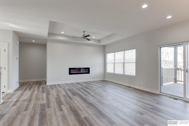 unfurnished living room featuring a raised ceiling, ceiling fan, and light hardwood / wood-style floors