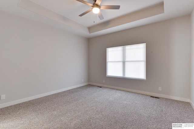 carpeted spare room with ceiling fan and a raised ceiling