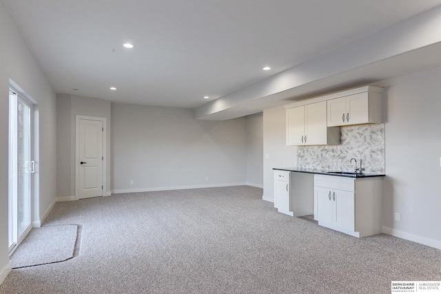 kitchen with decorative backsplash, light colored carpet, white cabinets, and sink