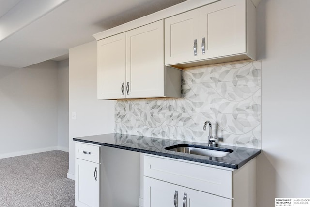 kitchen featuring dark stone countertops, white cabinets, backsplash, and sink