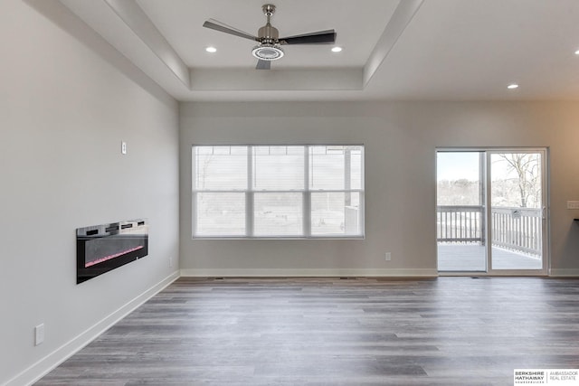 unfurnished living room with ceiling fan, a tray ceiling, heating unit, and hardwood / wood-style floors